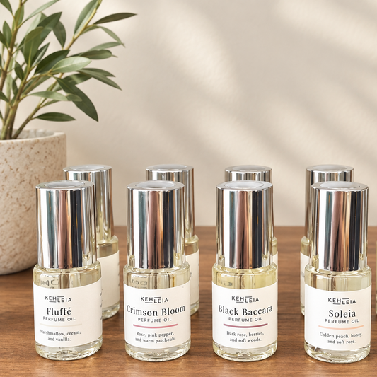 Small perfume oil bottles with silver caps and white labels arranged on a wooden surface. The labels read KEHLEIA and the scents Fluffe, Crimson Bloom, Black Baccara, and Soleia.